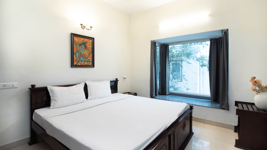 Hotel room with a double bed, white linen, a ceiling fan, and traditional wall art at Sanctum Suites Indiranagar, Bangalore.