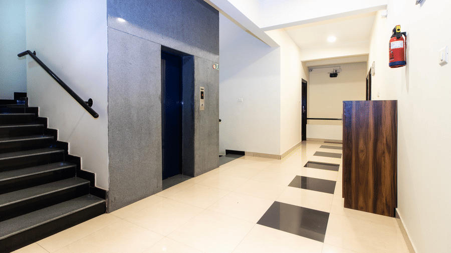 Hotel interior staircase with a clean corridor, tiled flooring, and a wooden door at Sanctum Suites Indiranagar, Bangalore.