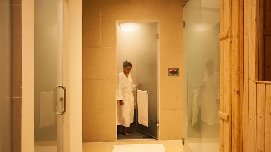 Person in a white robe standing in a shower, glass door, modern bathroom - Shreyas Retreat