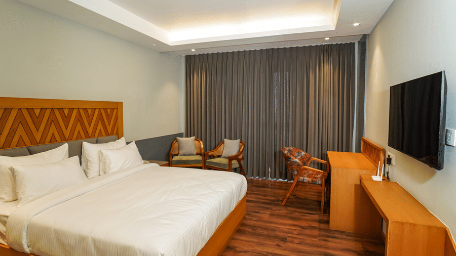 A bedroom showcasing a king size bed, a desk area with a chair, and a flat-screen TV on a stand | Sukama Resort & Spa, Mukteshwar