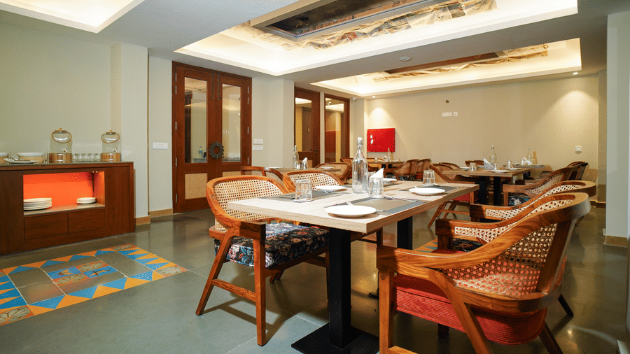 A dining room with several tables and chairs, a fireplace, and a large window | Sukama Resort & Spa, Mukteshwar