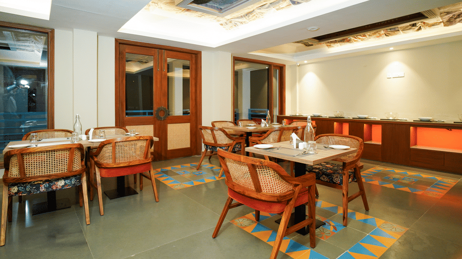 A dining area with multiple tables and chairs, featuring wooden accents and a patterned ceiling | Sukama Resort & Spa, Nainital