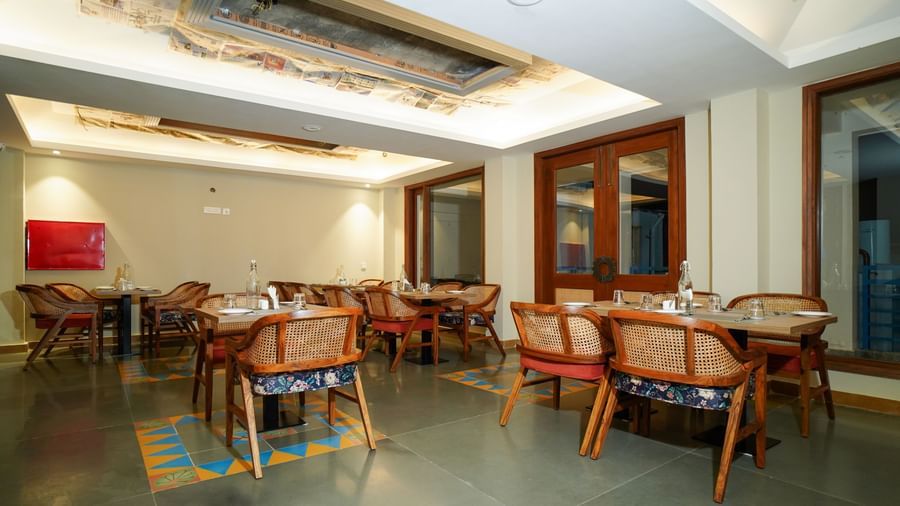 A spacious dining area with wooden tables and chairs, illuminated by overhead lighting and natural light from large windows | Sukama Resort & Spa, Nainital