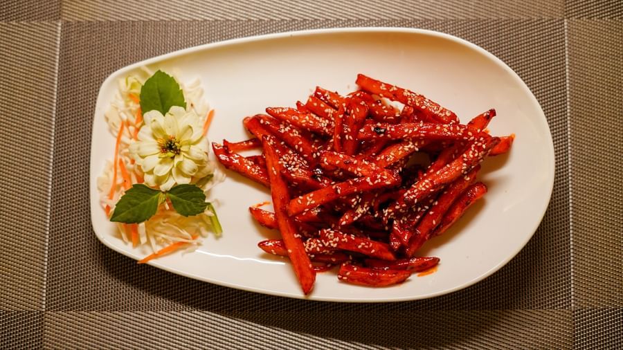 A white oval plate showcasing a serving of crispy red chili potatoes or a similar snack, accompanied by a small side salad | Sukama Resort & Spa, Nainital