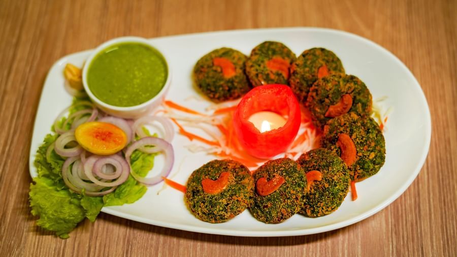A white platter presenting an array of round, green fried items, likely falafel or cutlets, served with various dips and a side salad | Sukama Resort & Spa, Nainital