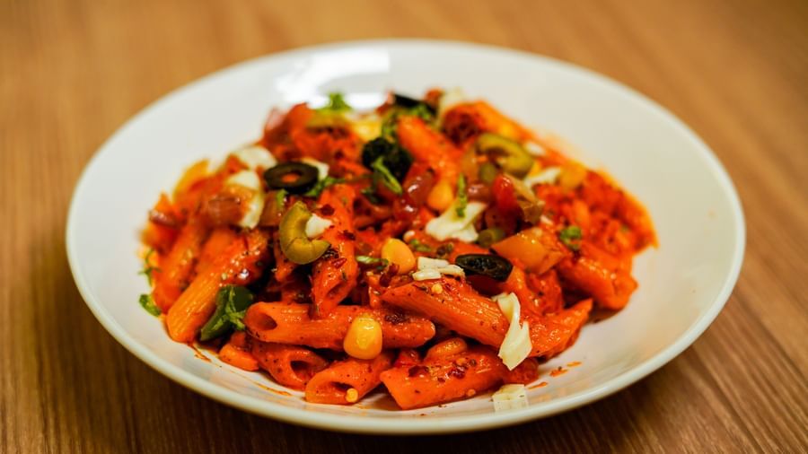 A white plate holding a vibrant pasta dish, possibly penne, tossed with colourful vegetables and sauce | Sukama Resort & Spa, Nainital