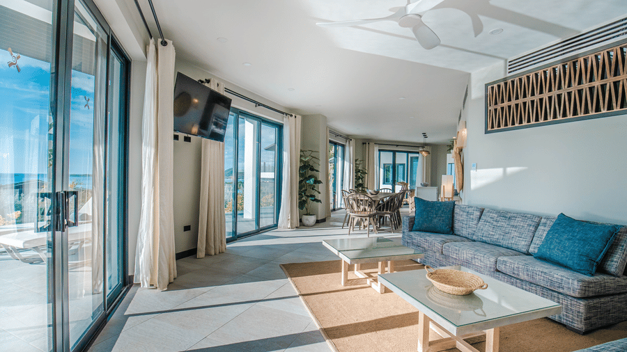 A living room with sofas, tables, and large windows overlooking the ocean at Tamarind Hills Resort and Villas, Antigua.