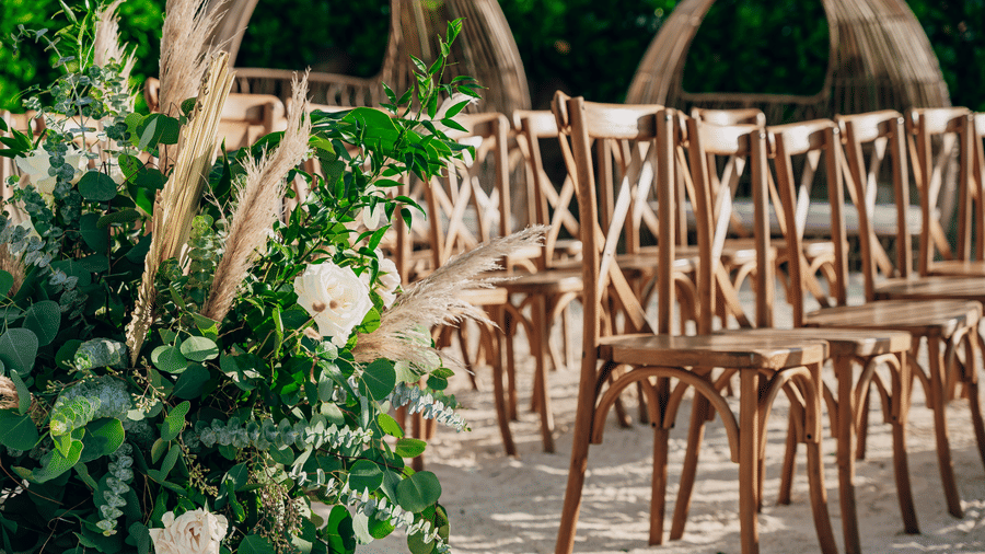 A row of wooden chairs arranged on sand beside green plants and white flowers at Tamarind Hills Resort and Villas, Antigua.