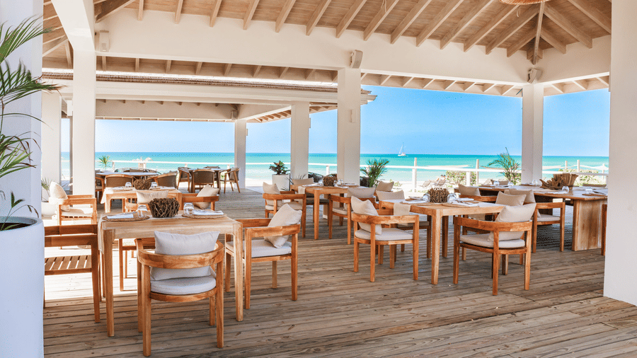 A beachfront dining area at Tamarind Hills Resort and Villas, Antigua, with multiple dining tables and chairs and ocean views.