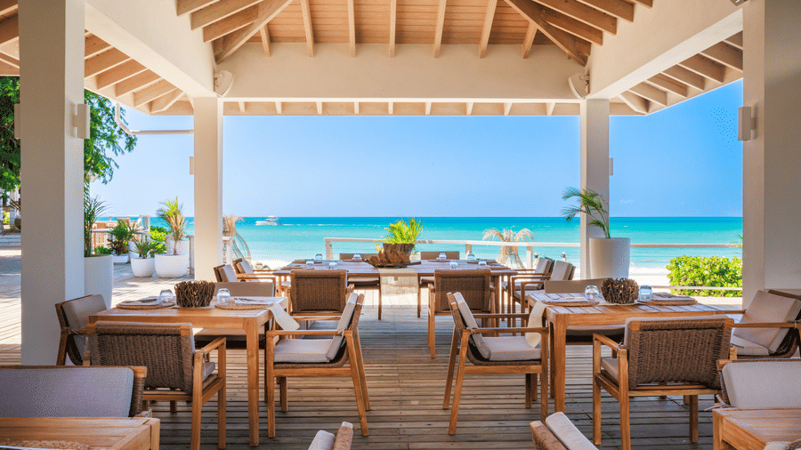 A beachfront dining area at Tamarind Hills Resort and Villas, Antigua, showcasing sea views and dining tables with chairs arranged.