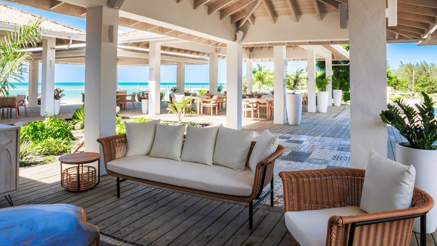 A sitting area with exposed beams, a sofa, a lounge chair, close to the dining area and with an ocean view at the Tamarind Hills Resort and Villas, Antigua.