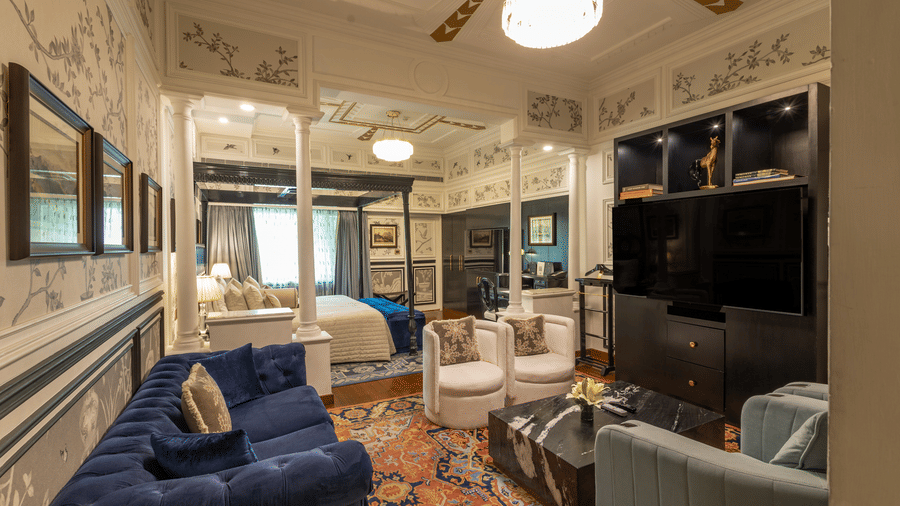 Side view of the Grand Luxury King Bed Room at The Claridges New Delhi, featuring a cosy sofa, wall-mounted TV, and elegant ceiling lights