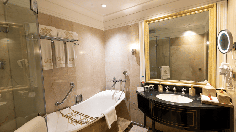 Grand Luxury Room washroom at The Claridges New Delhi, featuring a bathtub, a sleek sink, and a wall-mounted mirror