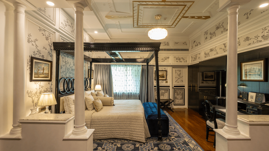 Grand Luxury Room at The Claridges New Delhi, showcasing a side view of the canopy bed with a bedside lamp and a chandelier