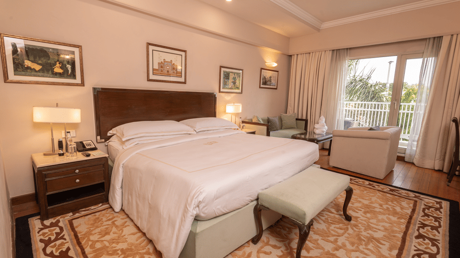 Luxury King Bed Room with Balcony at The Claridges New Delhi, featuring a cosy king sized bed with bedside lamps and a scenic view through a large window