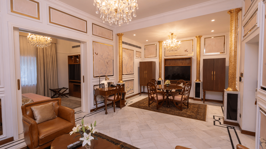 Luxury Suite at The Claridges New Delhi, featuring a spacious room with a corner sofa and a chandelier