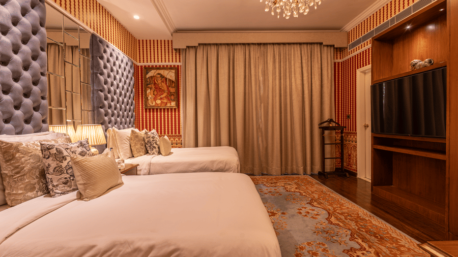 Side view of the spacious Luxury Twin Bed Room with Balcony at The Claridges New Delhi, featuring two separate beds, a stylish candellia hanging