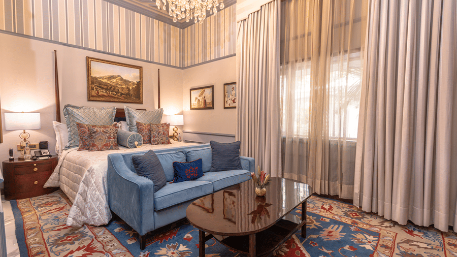 image of a luxurious bedroom from a corner angle of the heritage parlour suite with a king size bed and a coffee table in front of the bed - The Claridges New Delhi