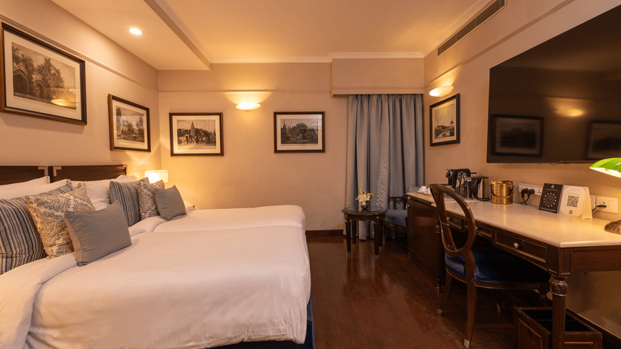 Side view of the Superior Twin Bed Room at The Claridges New Delhi, showcasing twin beds, a wall-mounted TV, and bedside lamps