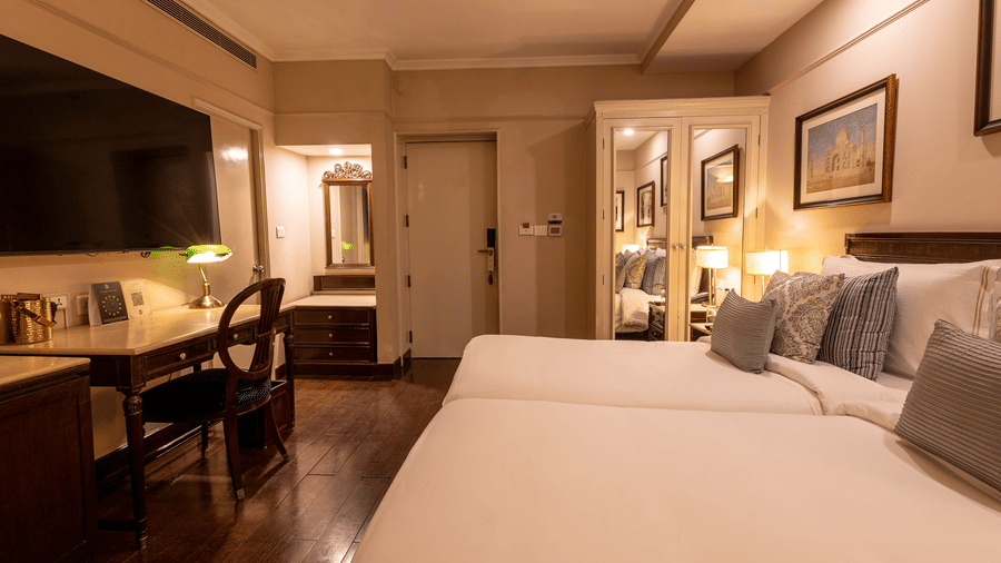 Side view of the Superior Twin Bed Room at The Claridges New Delhi, showcasing twin beds, a wall-mounted TV, and bedside lamps
