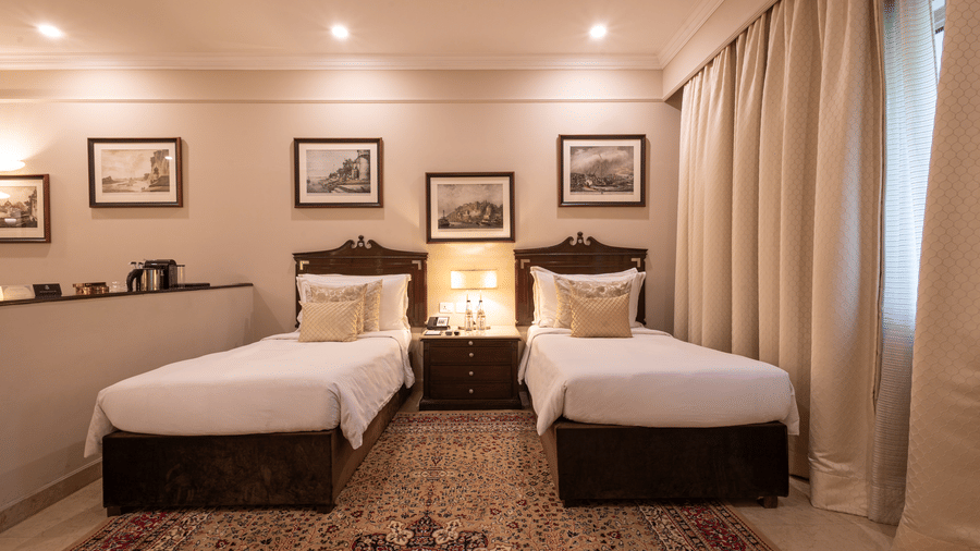 Front view of the Grand Luxury Twin Bed Room at The Claridges New Delhi, featuring elegant twin beds, a framed photo on the wall, and stylish ceiling lights