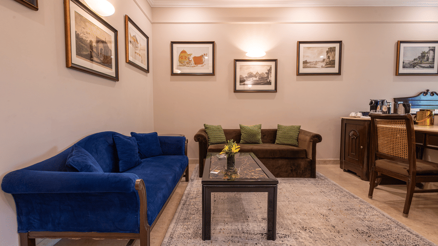 Corner view of the Grand Luxury Twin Bed Room at The Claridges New Delhi, featuring a cosy sofa with a table in front and framed photos on the wall