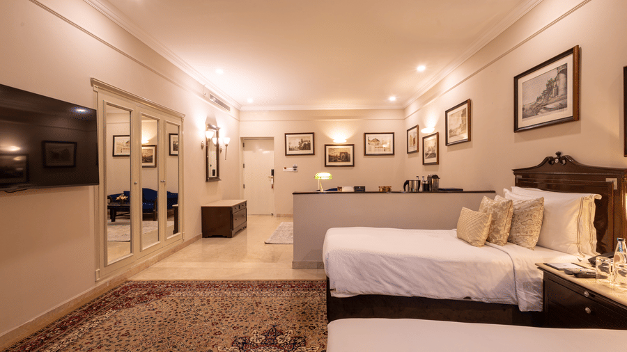 Side view of the Grand Luxury Twin Bed Room at The Claridges New Delhi, showcasing a spacious layout with framed photos on the wall and an elegant lighted ceiling