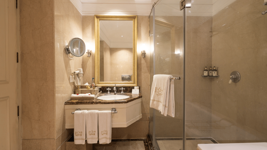 Washroom of the Grand Luxury Twin Bed Room at The Claridges New Delhi, featuring a modern sink, a wall-mounted mirror, and a glass-enclosed bath area
