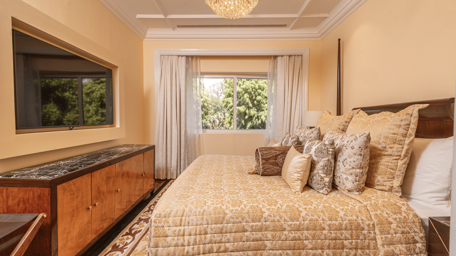  A luxurious king-size bed complemented by a wall-mounted TV positioned directly across from it in the Lutyens Luxury Suite at The Claridges New Delhi