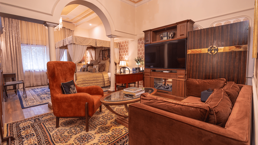image of the family seating area inside the bedroom of the heritage parlour suite with brown couch and a centre table in front of it with wall mounted tv - The Claridges New Delhi