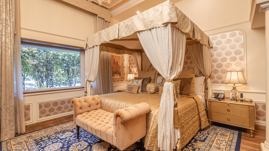image of the bedroom with a king size bed and thick curtain drapes around the bed giving a royal touch at our heritage parlour suite - The Claridges New Delhi