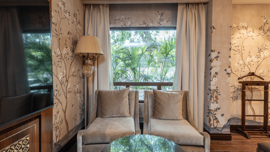 image of two single seater couch seats grey in colour with a huge window behind it at our cabana room - Image of the Cabana Room featuring two single-seater couches and a wall-mounted television - The Claridges New Delhi
