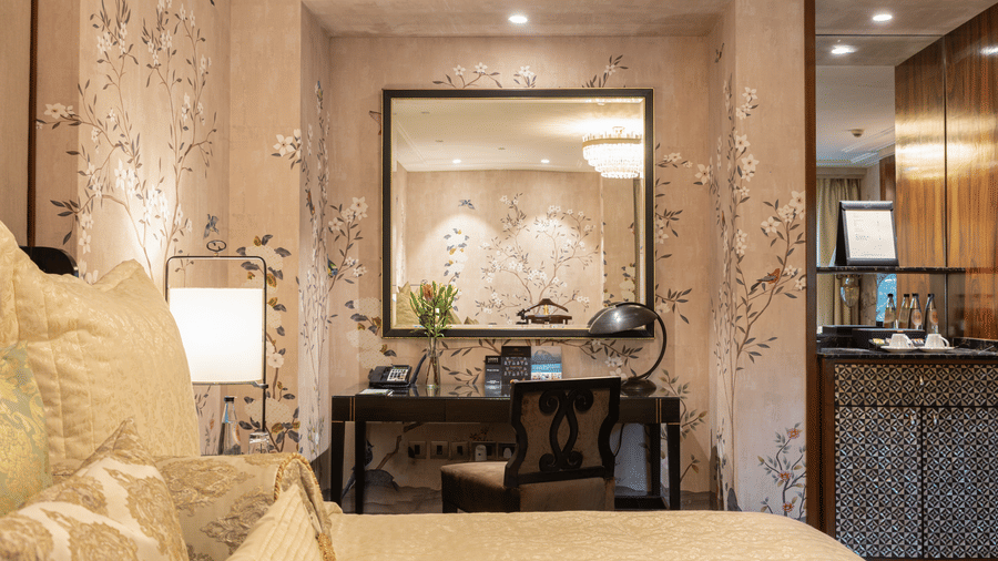 image of the work desk with a huge square shaped mirror above it giving an elegant touch to our caban room - Image of the Cabana Room featuring two single-seater couches and a wall-mounted television - The Claridges New Delhi