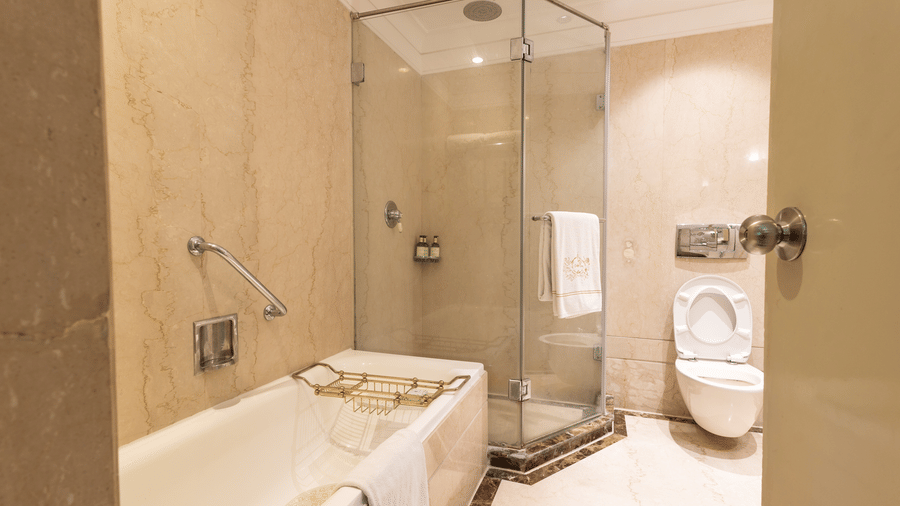 The bathroom in the Heritage Parlour Suite at The Claridges New Delhi, showcasing a cubical shower, a spacious bathtub, and a commode