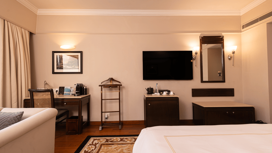 inside view of the heritage balcony room with a wall mounted tv in the middle, and a mirror along with a work desk besides it - The Claridges New Delhi