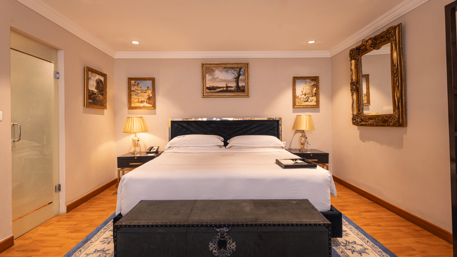 image of the bedroom with a plush king sized bed with table lamps at both sides of the bed at our regent suites - The Claridges New Delhi