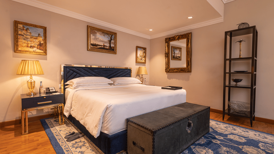 image of the bedroom with a soft comfortable bed with a wooden trunk in front of the bed at our regent suites - The Claridges New Delhi