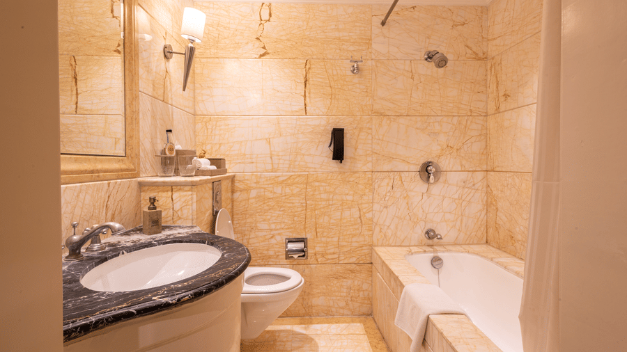 image of a well appointed bathroom with a wash basin and bathtub and a commode at the far corner of out heritage parlour room -The Claridges New Delhi