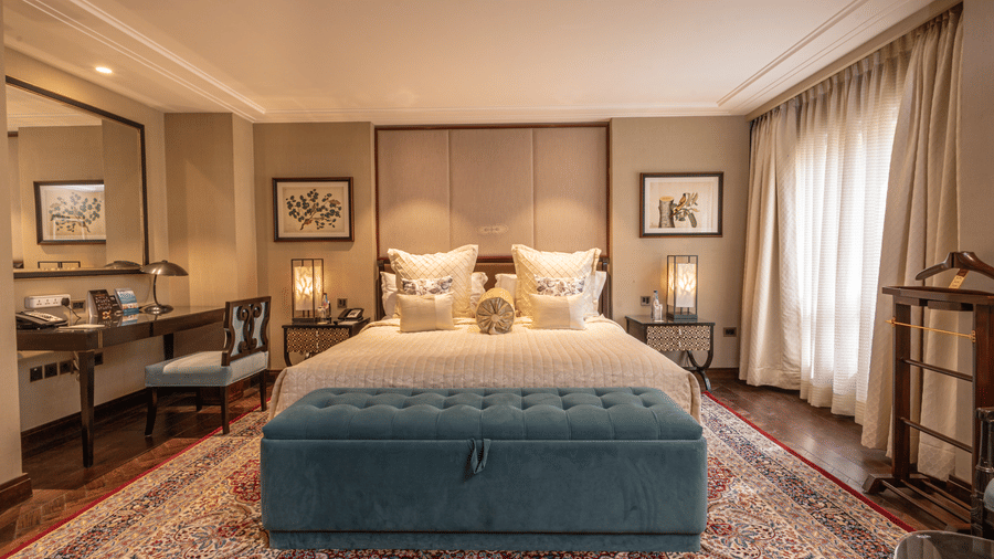 image of the caban room with beautiful interiors featuring a king size bed and the blue seating space in front of the bed - The Claridges New Delhi