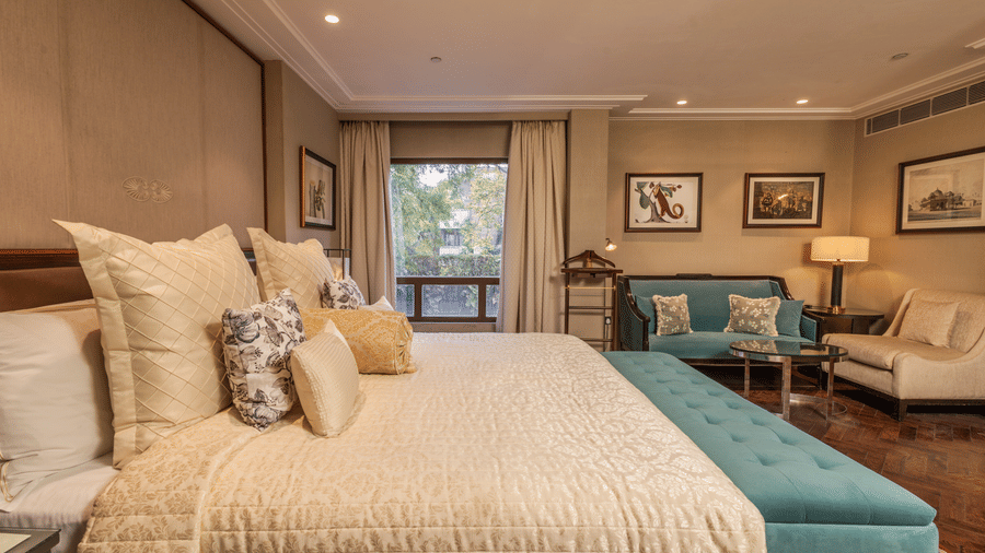 image of a plush king size bed with a soft comforter spread over it with a window at the cabana room - The Claridges New Delhi