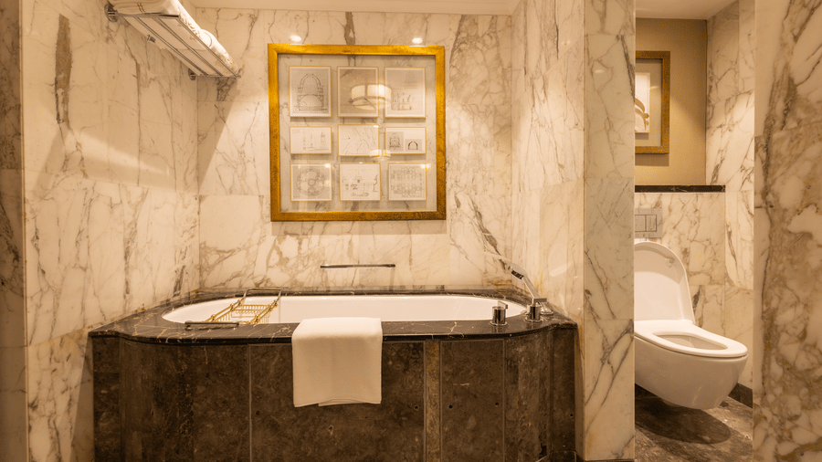 image of a luxurious bathtub with a huge golden photo frame over it at our cabana room - Image of the Cabana Room showcasing exquisite interiors, including a king-size bed and a stylish blue seating area positioned in front of the bed at The Claridges New 