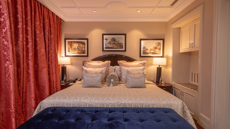image of the bedroom with red curtains in the room and a blue seating space in front of the bed at our regent suite - The Claridges New Delhi