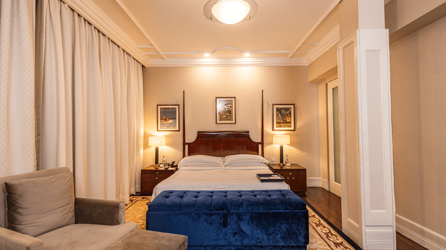 front view of the bed with a blue cushioned seating structure in front of it at our heritage room - The Claridges New Delhi