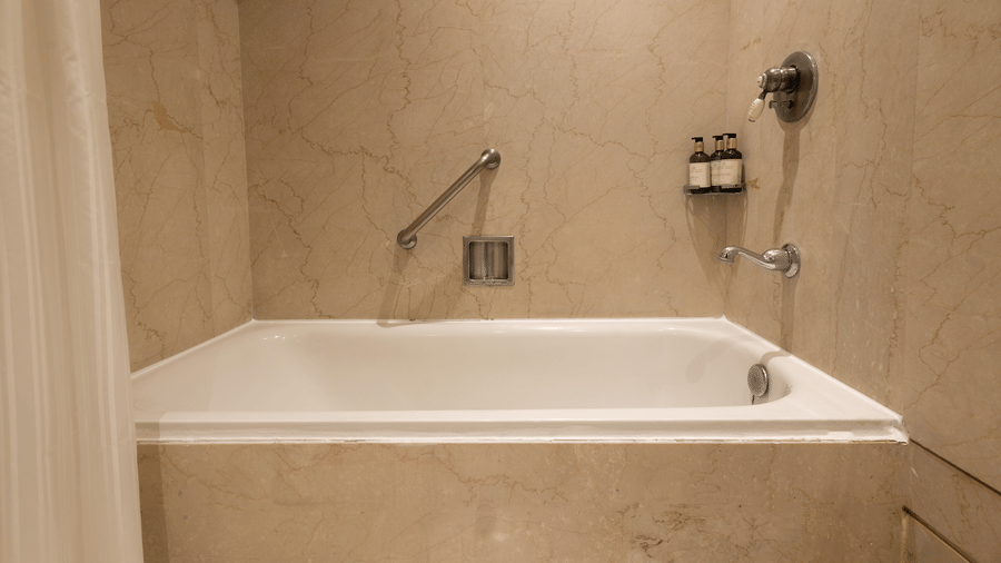 image of a bathtub with a curtain at our heritage balcony room with beige tiles -The Claridges New Delhi