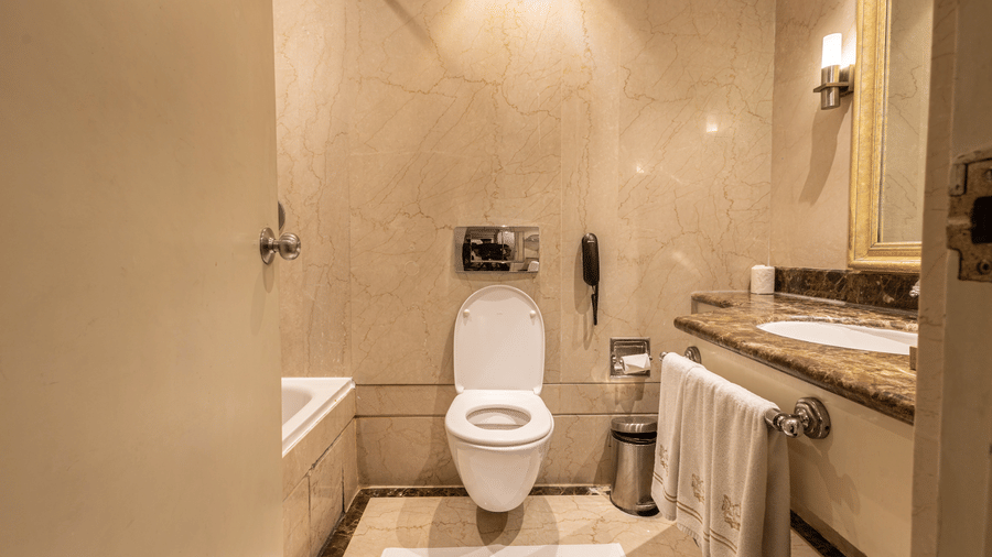 image of the bathroom with a commode and a wash basin with a hanging clean white towel at our heritage balcony room - image of the heritage balcony room with sleek interiors and a a plush king size bed - The Claridges New Delhi