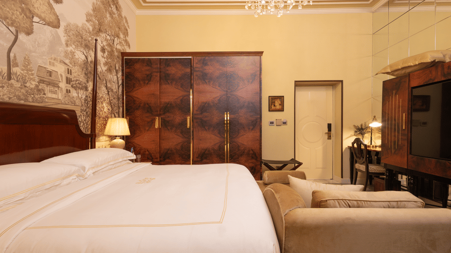 image of the heritage room featuring a soft king size bed with hardwood wardrobe besides it - The Claridges New Delhi