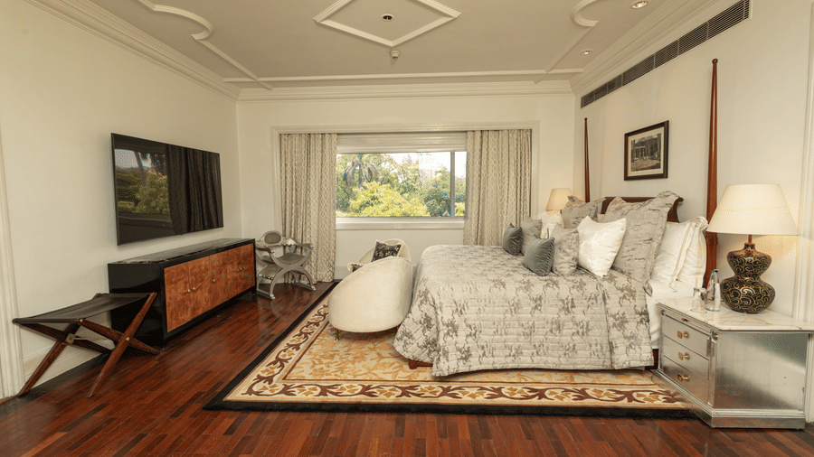 full view of the bedroom with a king size bed with well set pillows on it and a wall mounted tv screen opposite the bed at our viceroy house estate suite - The Claridges New Delhi