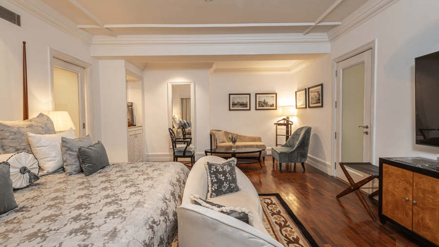 an image of our viceroy house estate suite showcasing the king size bed with modern interiors and a seating area at the far corner of the suite - The Claridges New Delhi
