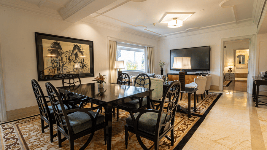 The living area and dining table of the Viceroy House Estate Suite at The Claridges New Delhi are featured in the image from a corner perspective