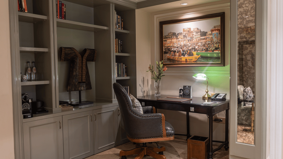 a study area with a well segregated grey cabinets beside the desk - Two chairs, accompanied by a small coffee table, are placed in the middle of the room at The Claridges New Delhi.